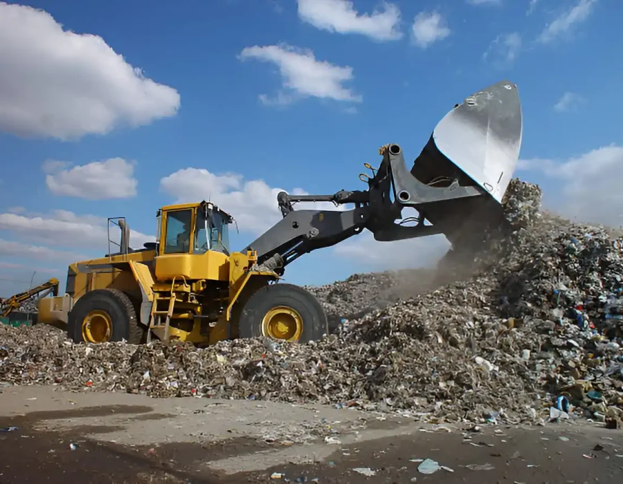 Yellow wheel loader with large bucket moving and managing construction debris at landfill site