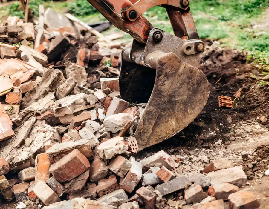 Close-up of excavator bucket moving brick and concrete rubble during demolition cleanup process