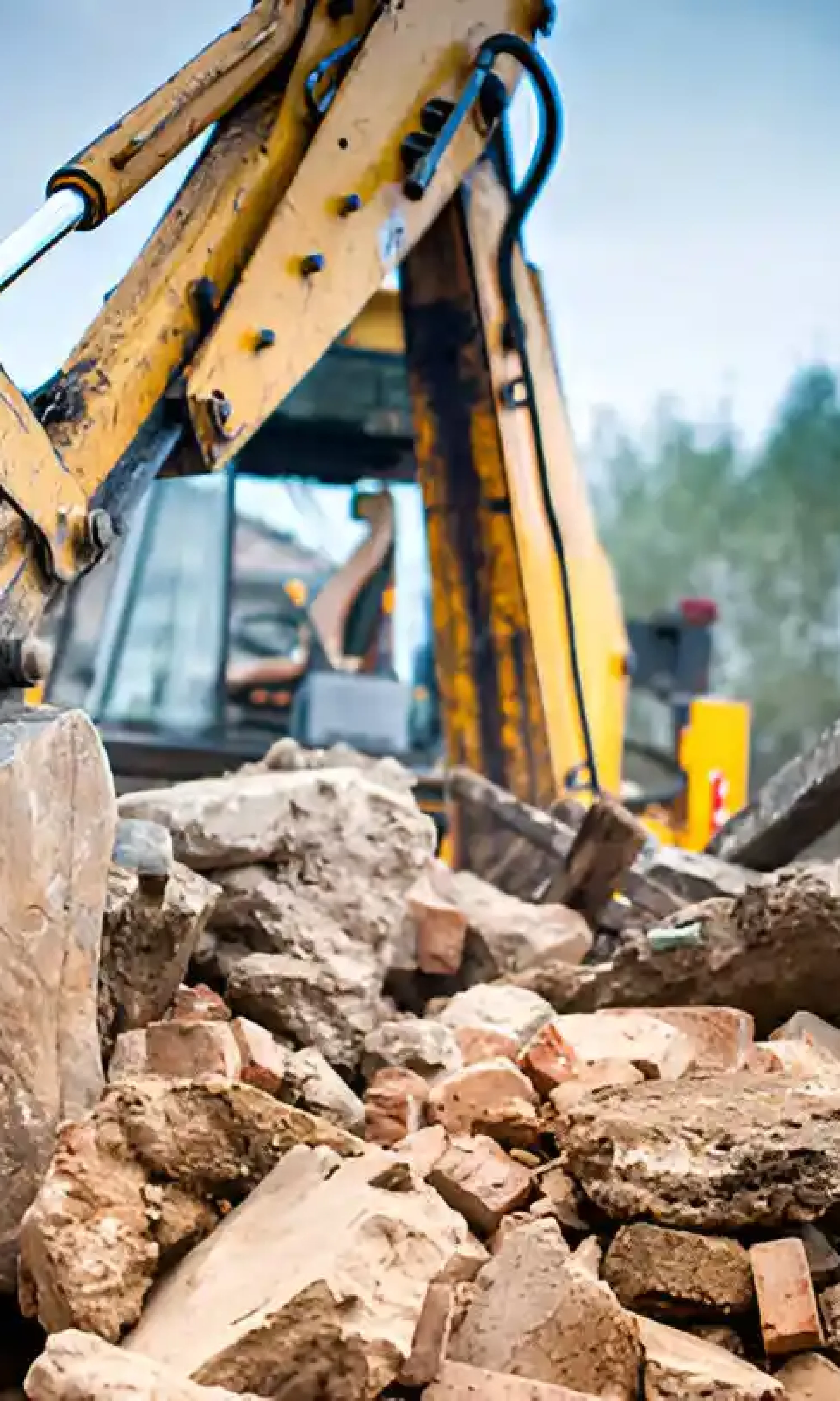 Heavy-duty excavator with bucket clearing demolition debris and concrete rubble at residential worksite