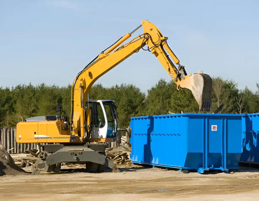Yellow excavator loading construction waste into blue roll-off containers at industrial demolition site
