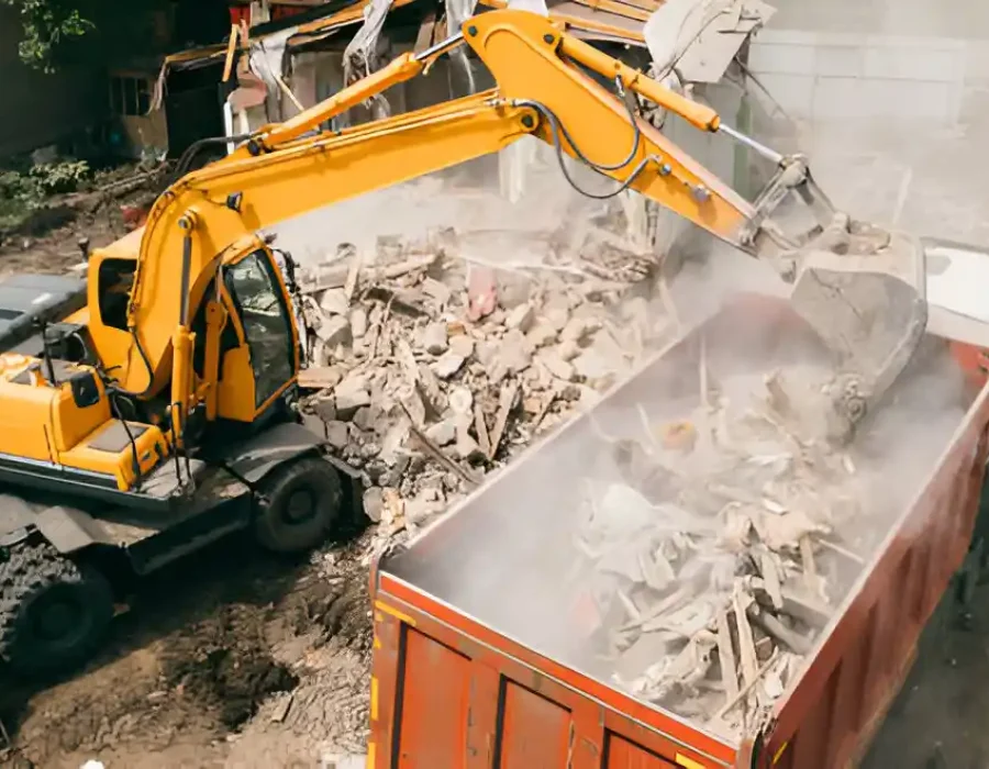 ellow excavator transferring demolition waste into orange dump truck at residential cleanup site