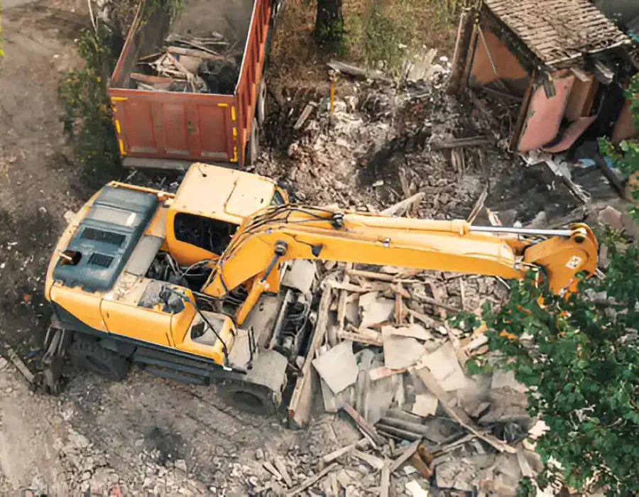 Aerial view of yellow excavator clearing demolition debris next to dumpster at construction site