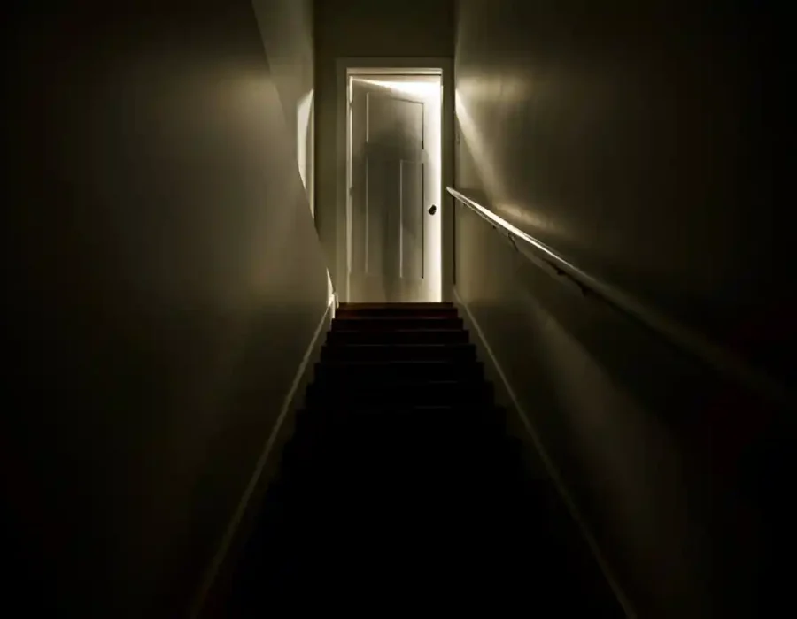 Dark staircase with light shining through a partially open door at the top.