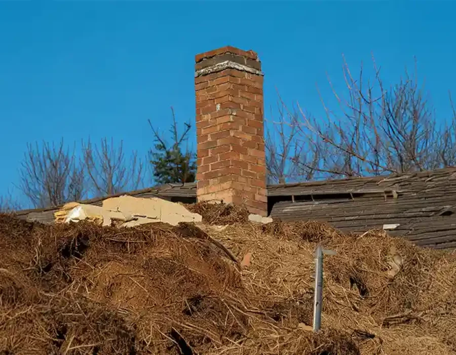 Collapsed roof with brick chimney on demolition site debris.