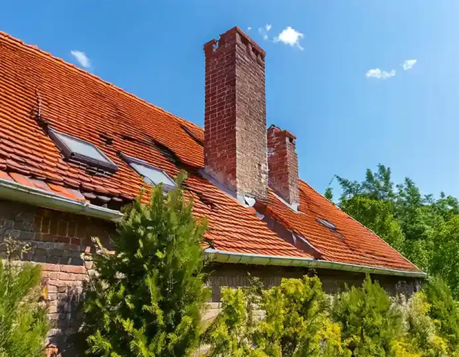 Old building with damaged roof tiles and chimney, set for demolition and debris removal.