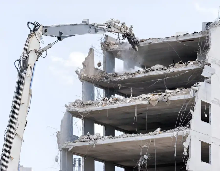 White excavator dismantling multi-story concrete building floor by floor