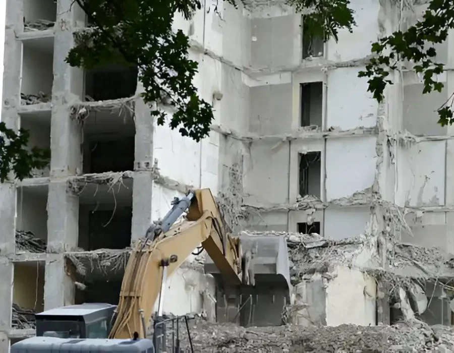 Excavator dismantling multi-story white concrete structure with systematic demolition