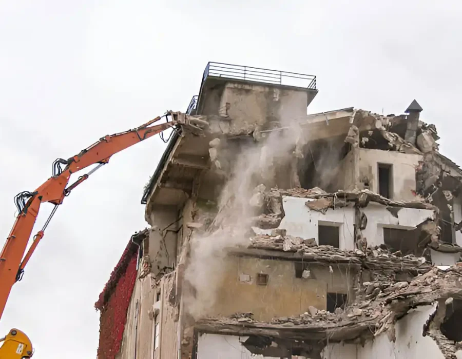 Orange demolition crane dismantling concrete building with active dust control measures