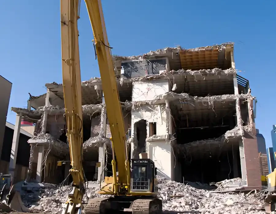 Industrial demolition machine removing concrete building, debris cleanup in progress