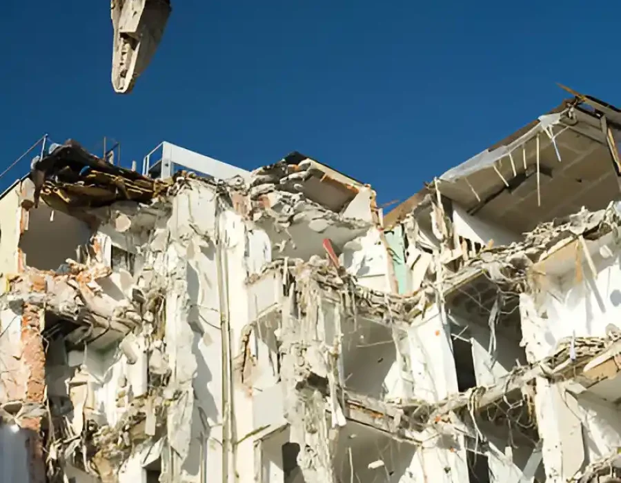 Excavator demolishing white concrete building, exposed floors and structural damage