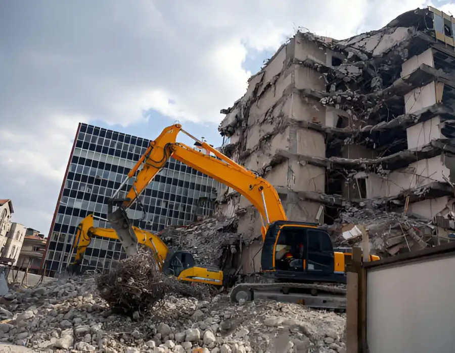 Yellow excavator dismantling multi-story concrete building, massive debris pile below