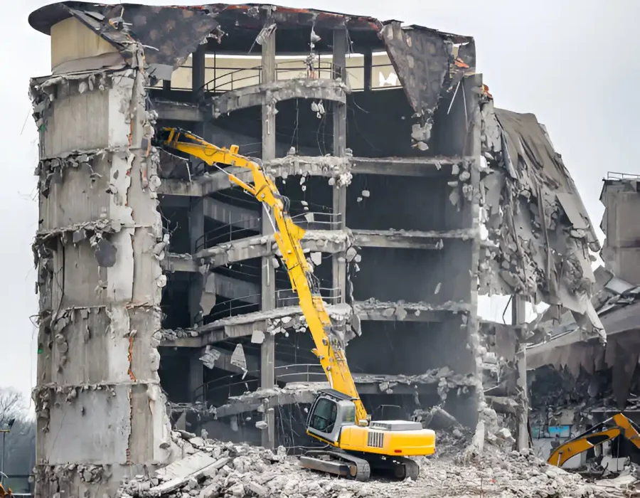 Yellow excavator dismantling concrete building, exposed structural floors and debris