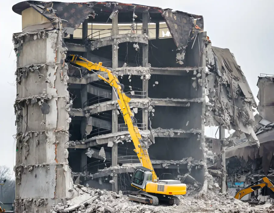 Long-arm excavator demolishing concrete structure showing exposed floors and building framework