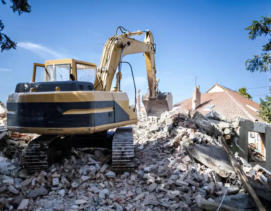 Excavator removing rubble and debris from a residential demolition site under clear skies.