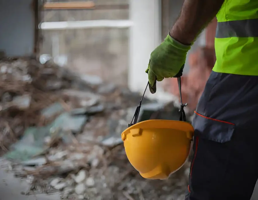 Worker holding yellow helmet near debris at demolition site.
