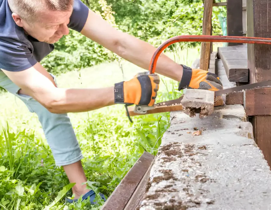 Worker using saw to dismantle wooden structure outdoors