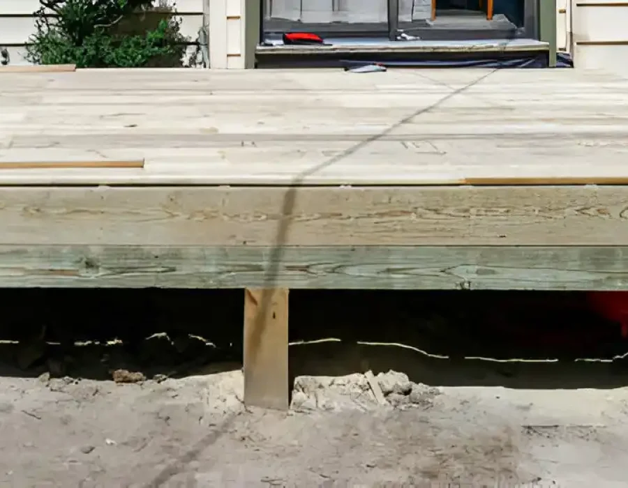 Partially removed wooden deck with exposed support beams and tools.