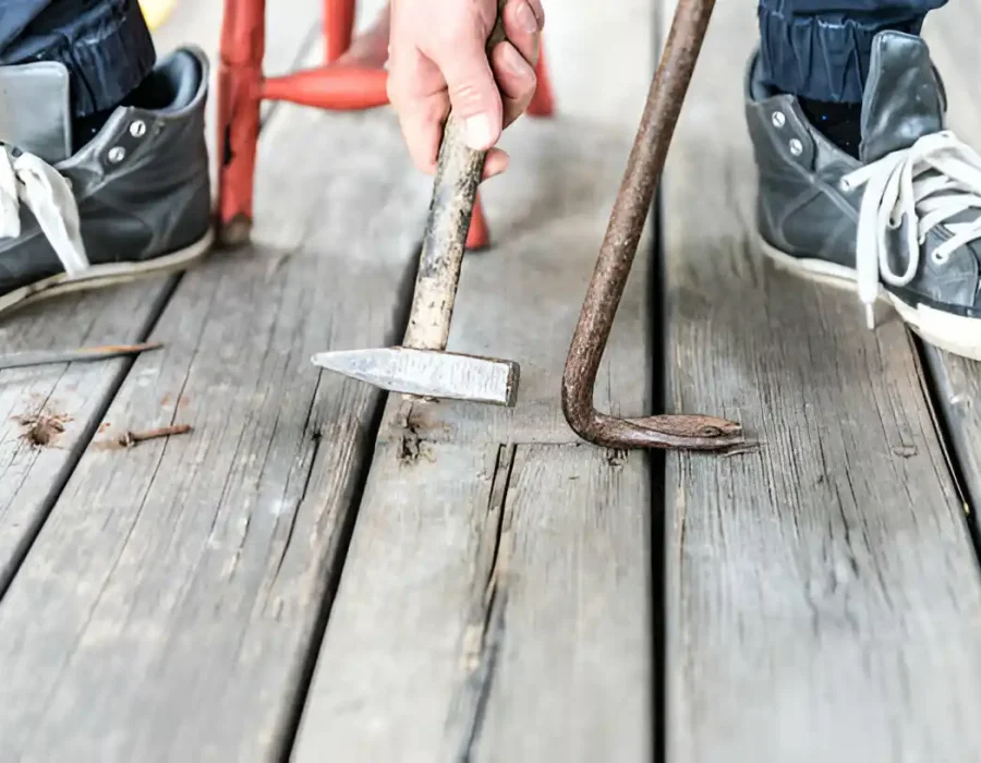 Close-up of deck board removal using crowbar and hammer.