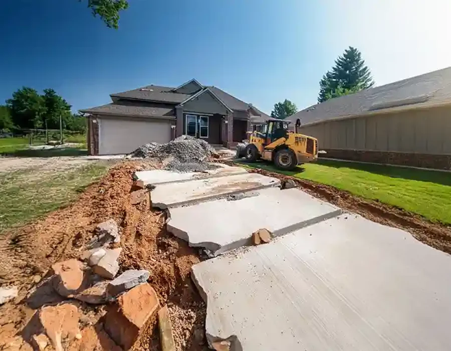 Broken concrete driveway with heavy equipment for demolition and site preparation in a residential area.