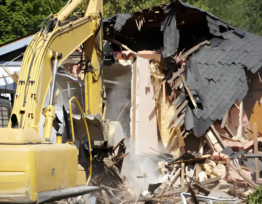Excavator tearing down a house during a demolition project amidst debris and rubble.