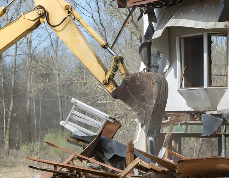 Excavator tearing down home structure with debris scattered around.