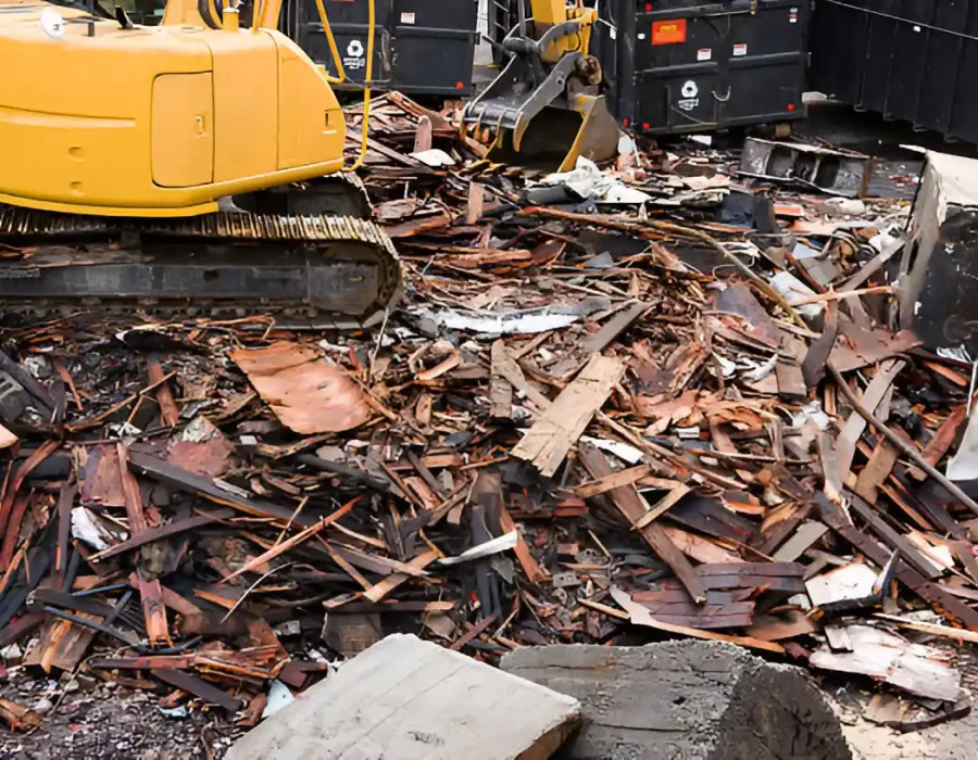 Yellow excavator at a demolition site clearing wood and debris into disposal containers.