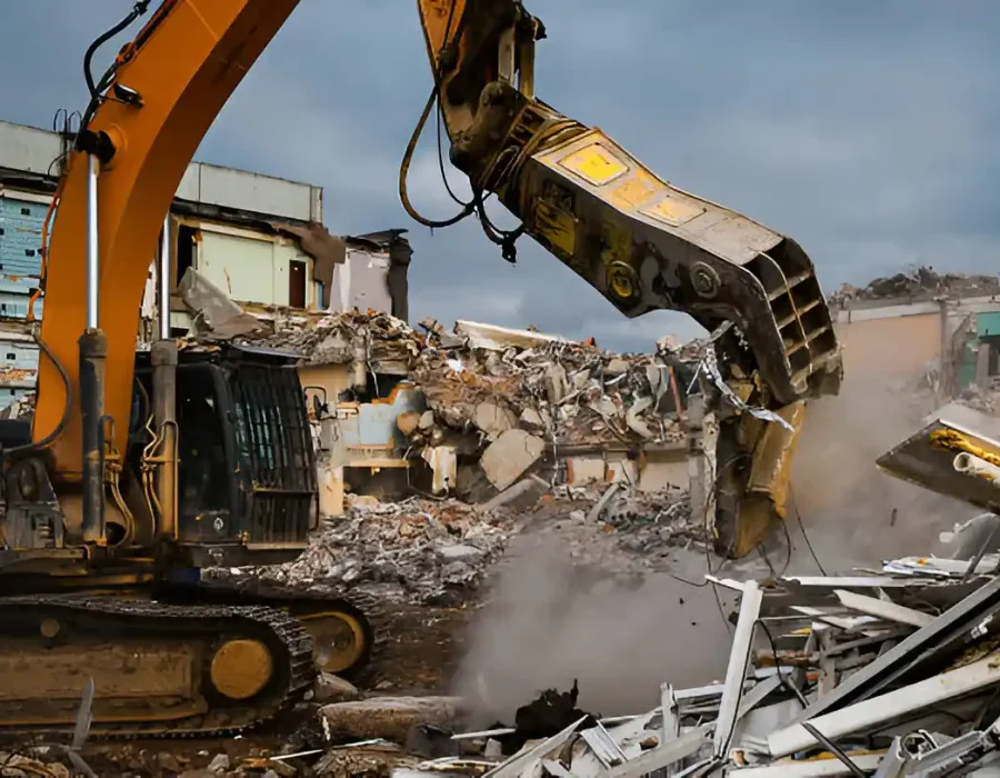 Yellow excavator tearing down a building, surrounded by rubble and debris at a demolition site.