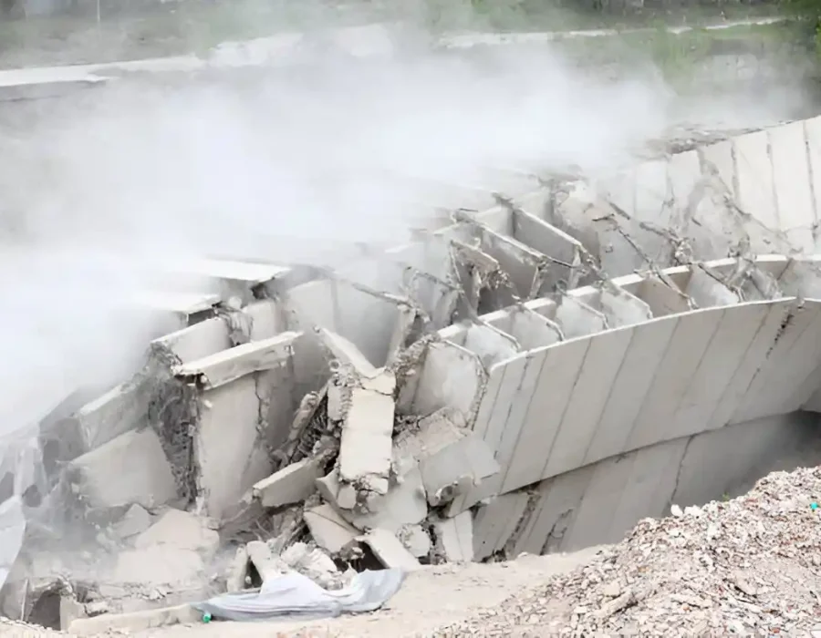 Large concrete structure crumbling during controlled demolition, dust and debris visible