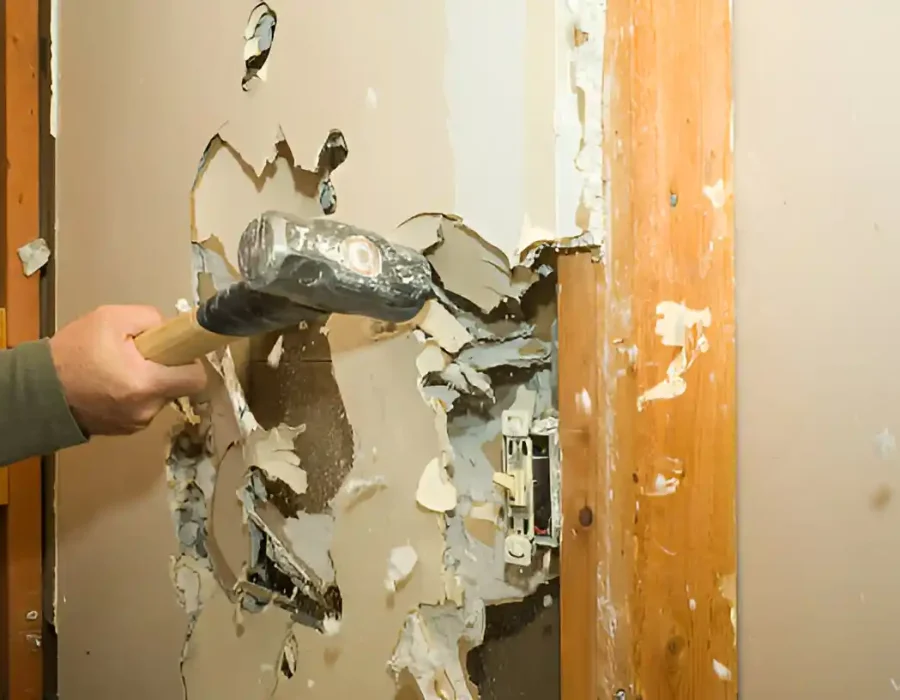 Hammer breaking through drywall, exposing electrical box during renovation project