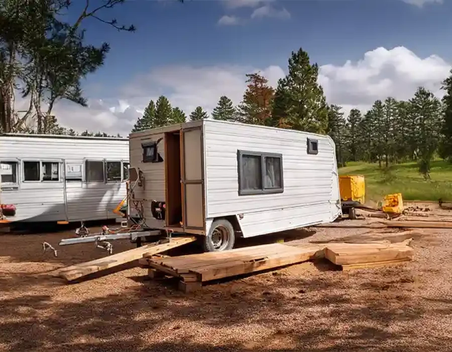 Two white trailers with lumber supports and equipment at forest construction clearing site