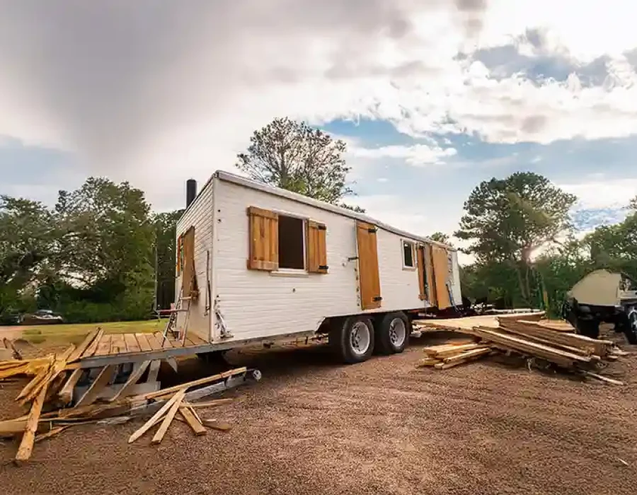 White trailer with wooden shutters surrounded by scattered lumber debris on prepared demolition site