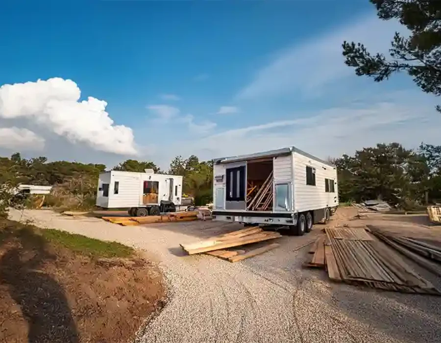 Two mobile homes on gravel clearing with scattered lumber at hillside demolition location