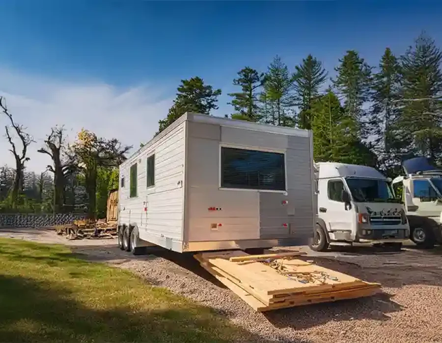 White construction trailer with lumber debris and utility trucks at forested demolition site setup
