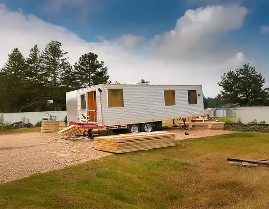 Construction trailer with stacked lumber and cleanup materials on prepared site with concrete walls