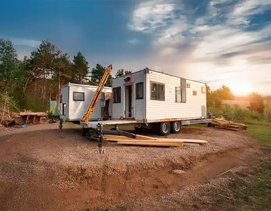 Mobile home with stabilizers and construction waste at sunset demolition site with forest backdrop