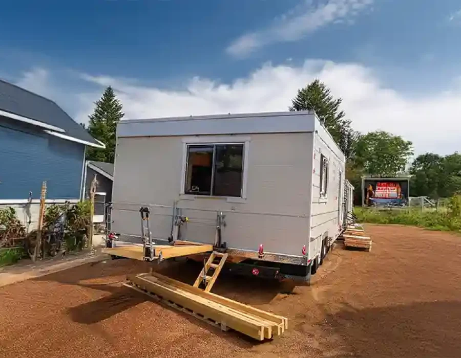 White trailer with leveling equipment and lumber debris near blue building at construction site