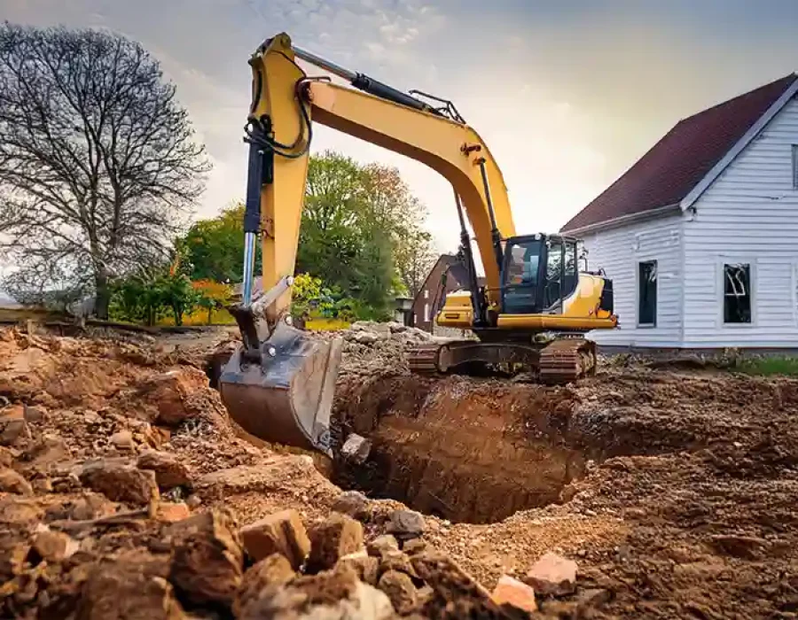 Excavator digging soil near a house for site preparation and construction.