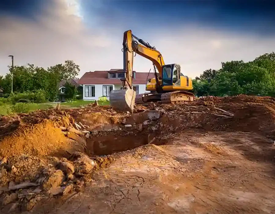 Excavator digging soil near a house for demolition and site preparation services.