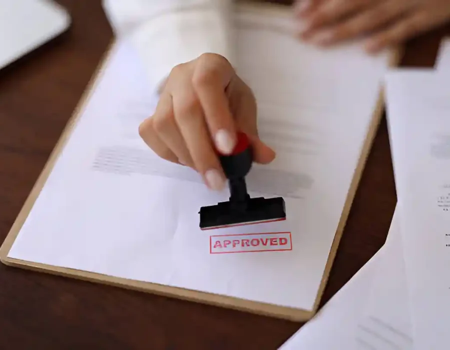 Hand stamping approved on demolition permit paperwork with red ink on wooden desk for site clearance
