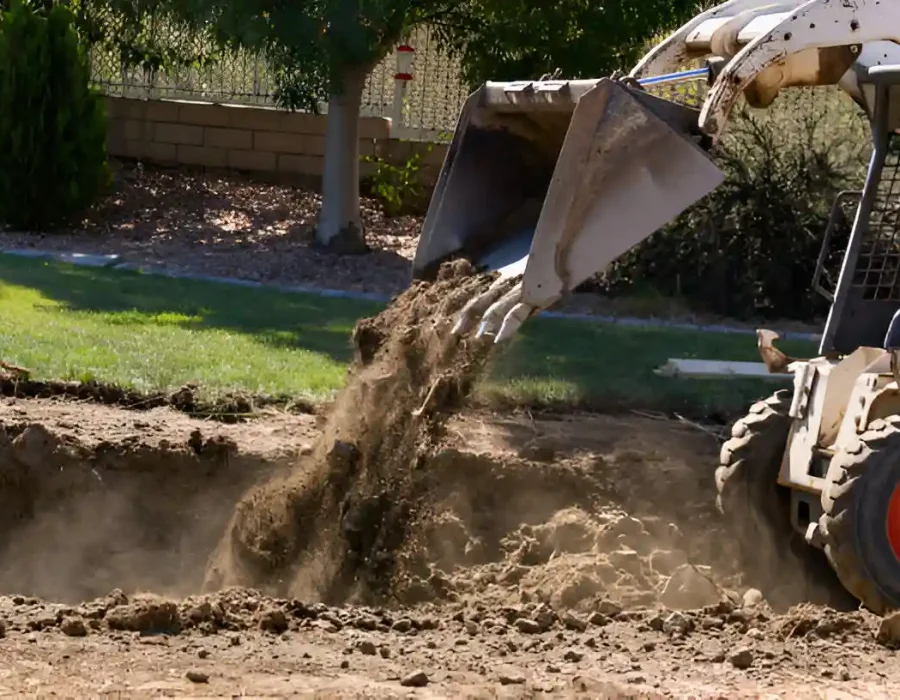 Bobcat excavator removing soil during residential demolition and site preparation project in backyard setting