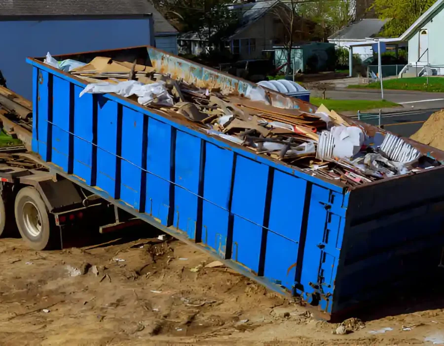 Large blue industrial dumpster filled with construction debris at residential demolition site