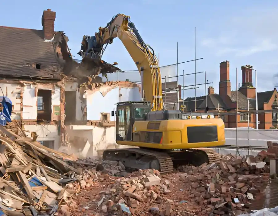 Heavy excavator demolishing brick house with debris pile during commercial demolition project in urban area