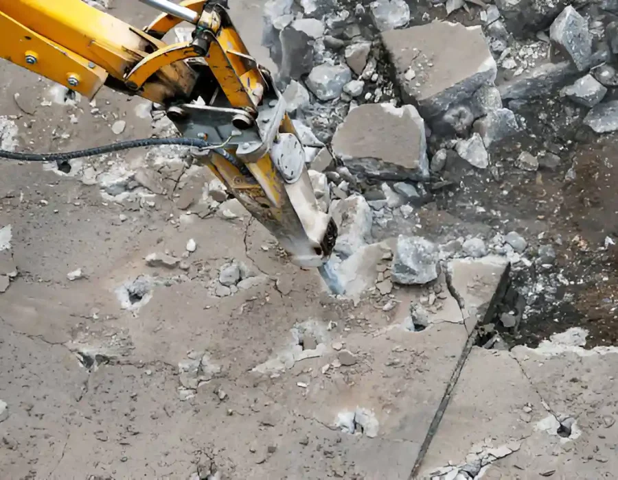 Heavy-duty hydraulic breaker demolishing concrete surface with debris, showcasing professional demolition services
