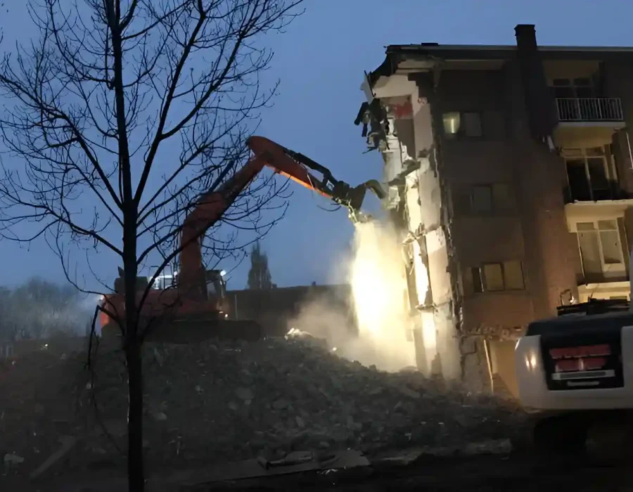 Excavator demolishing building at night with debris
