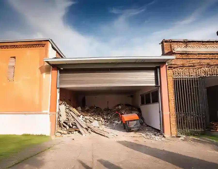 Partially demolished garage filled with rubble and debris, with a wheelbarrow in front of the site.