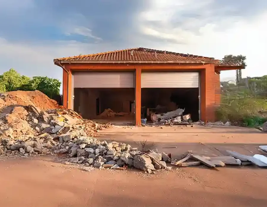 Partially demolished garage with rubble, dirt, and debris piles scattered in front of the structure.