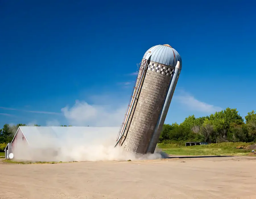 Falling silo being demolished, creating dust cloud on a sunny day.