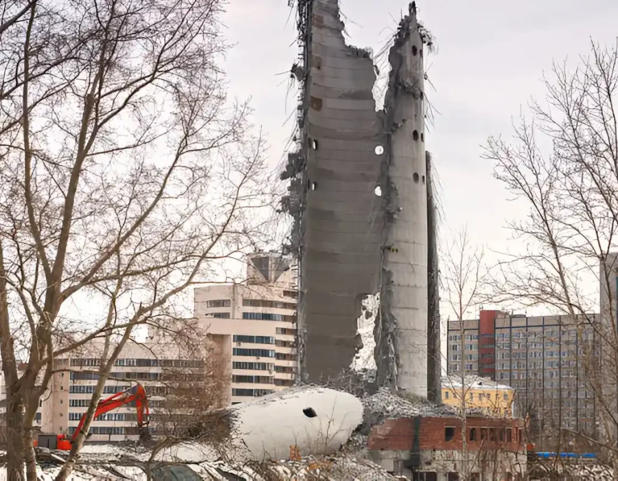 Partially demolished concrete structure with debris and an excavator on an urban demolition site.