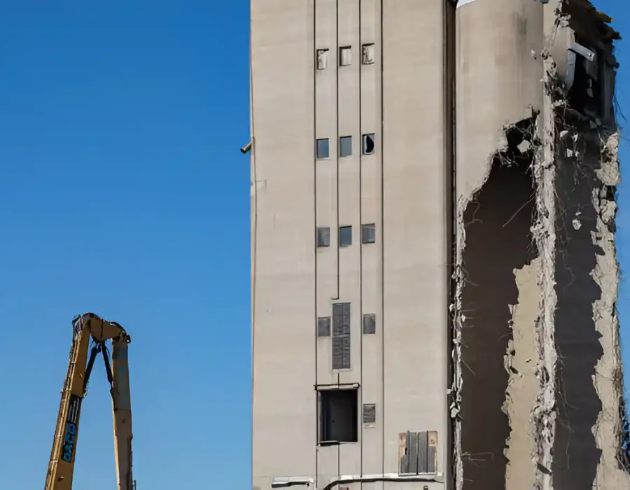 Excavator demolishing a concrete building under a clear blue sky.