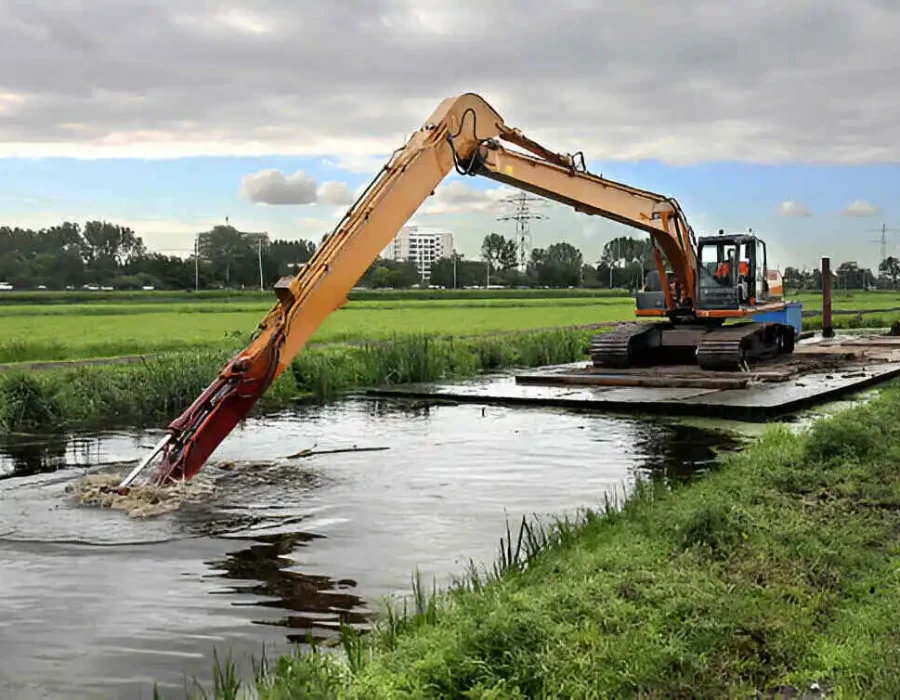 Excavator on floating platform clearing water channel, removing sediment in wetland